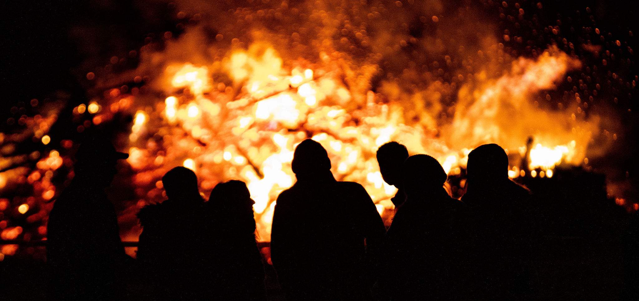 a group of people standing in front of a fire.