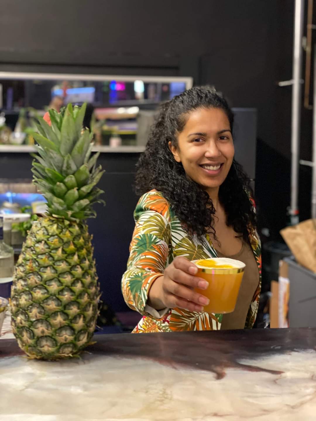 a woman holding a cup of juice next to a pineapple.