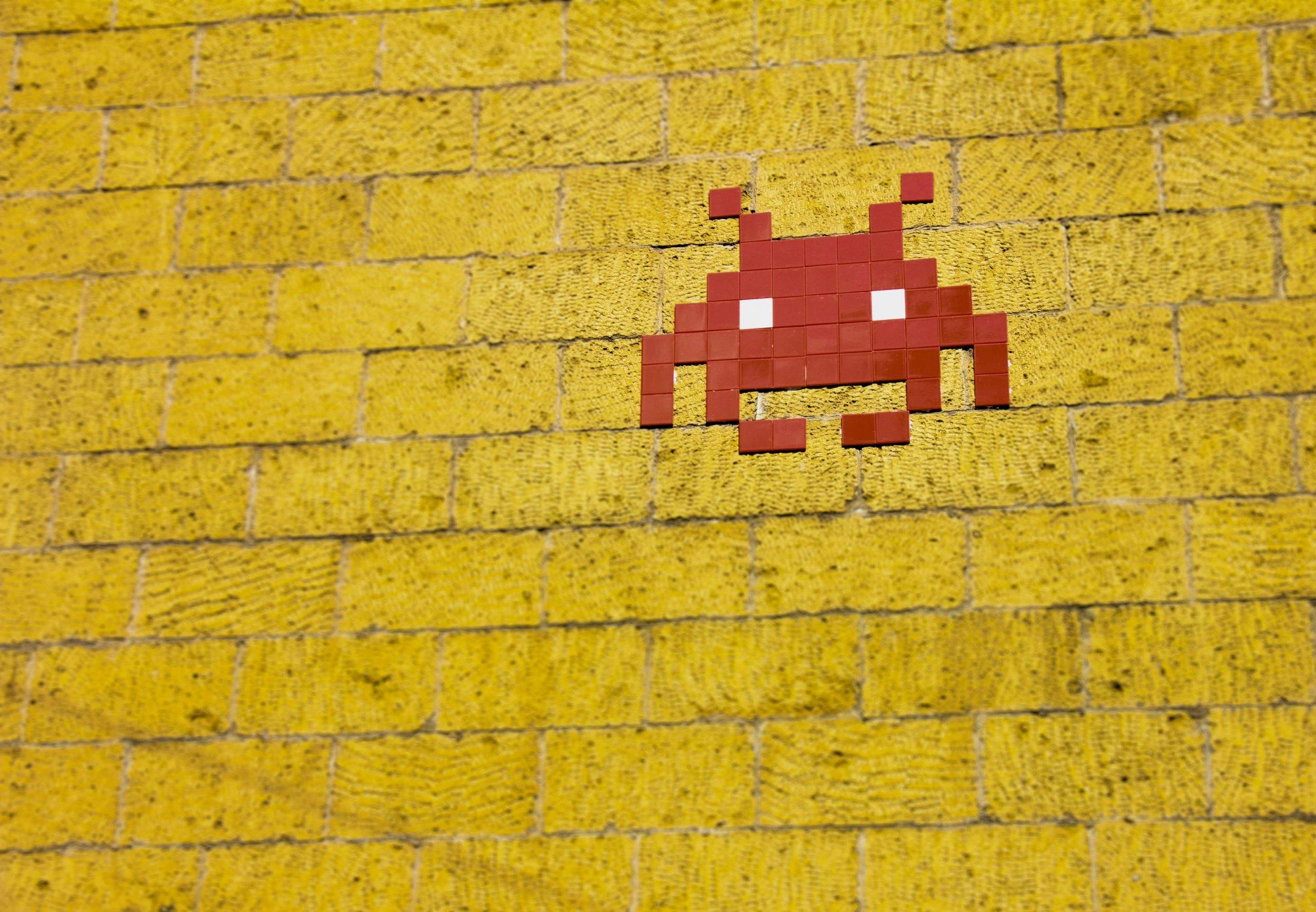 a brick wall with a sticker of a red space invade on it.