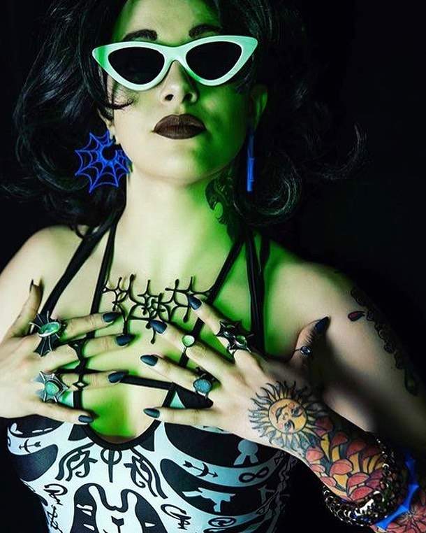 a woman with green makeup and tattoos holding her hands together.