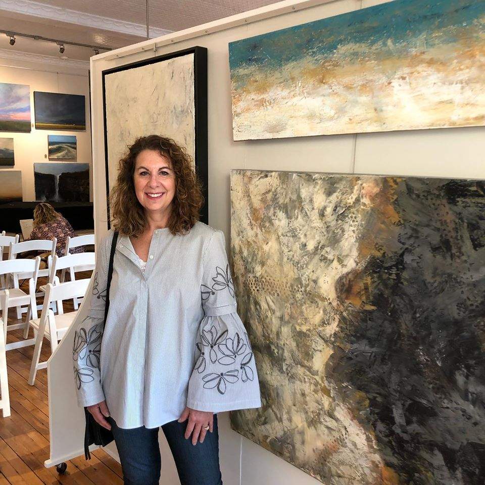 a woman standing next to some paintings in a room.