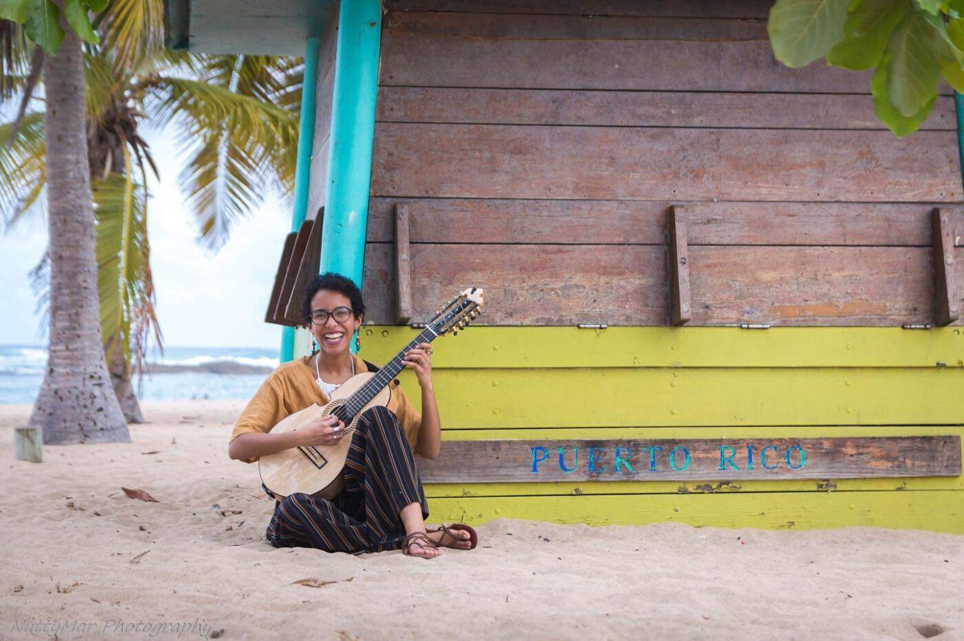 a man sitting on the beach playing a guitar.