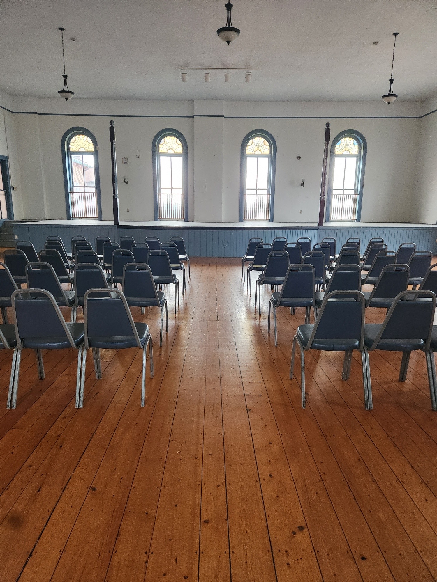 Sunlit room at Salem Playhouse with gleaming wood floors and rows of gray chairs, ready to spark creative community in Essex County.