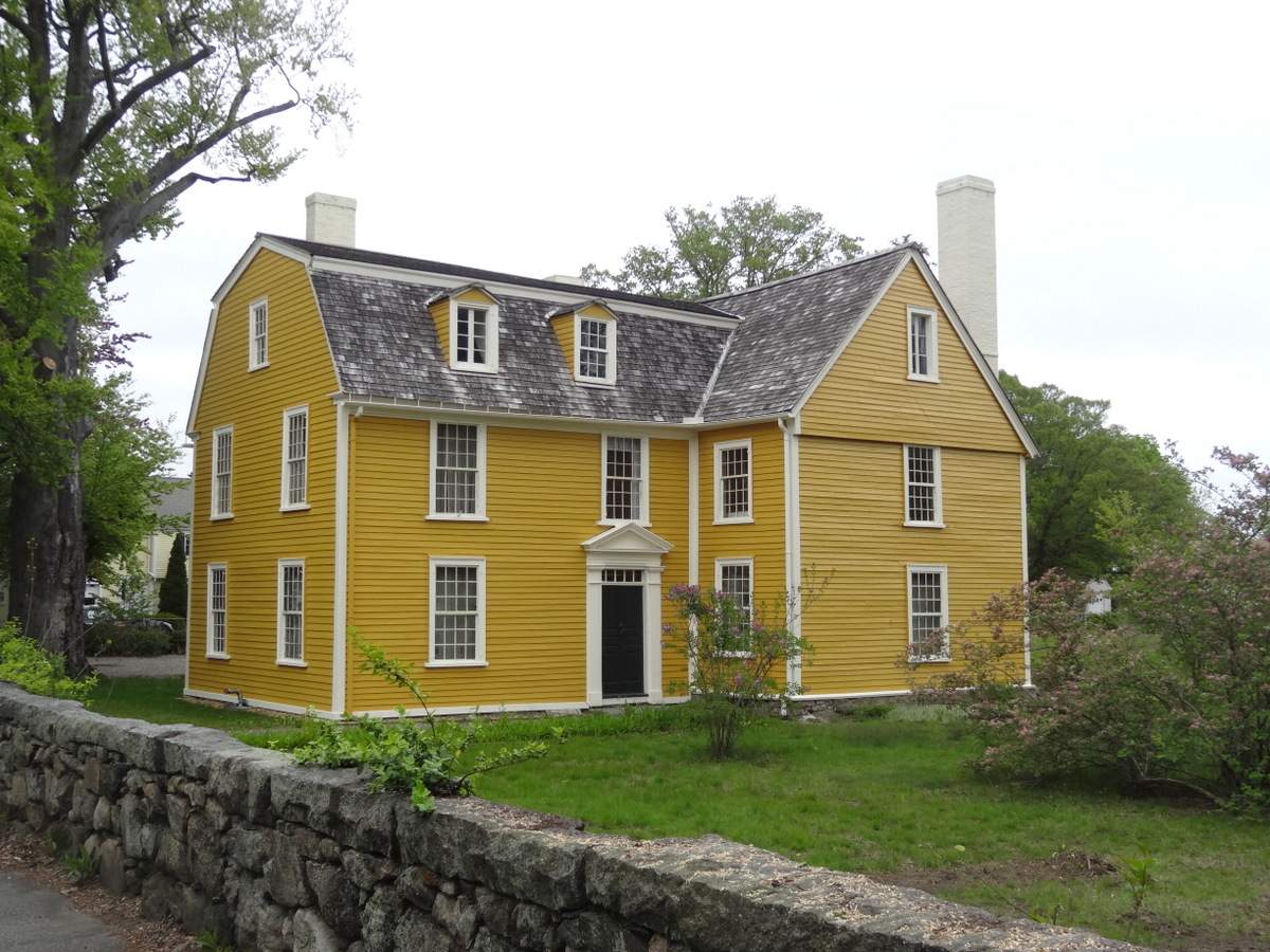 a large yellow house with a stone wall in front of it.