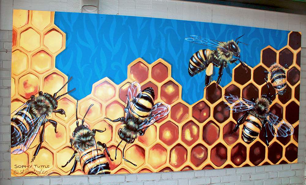 a painting of bees and honeycombs on a brick wall.