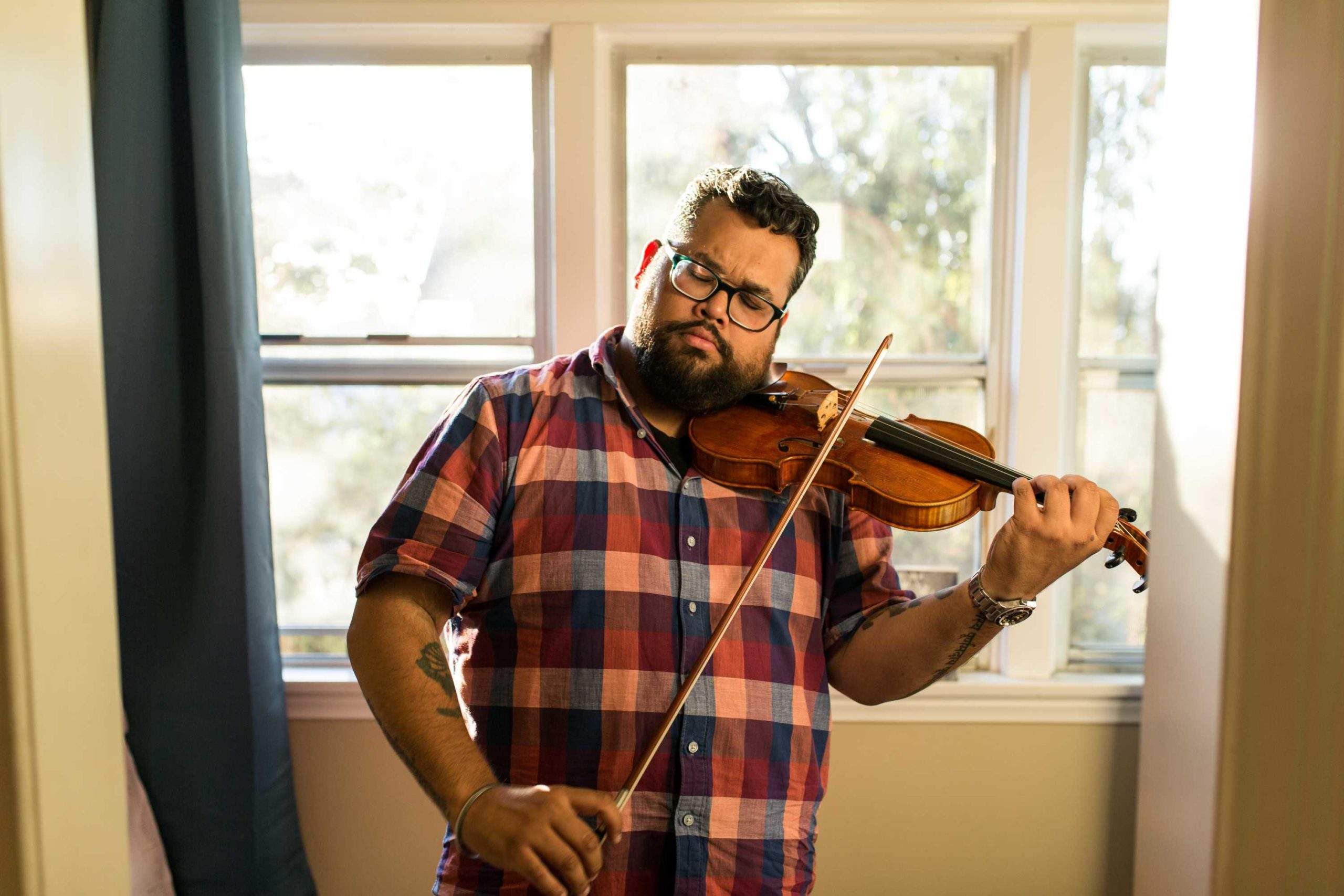 a man playing a violin in front of a window.