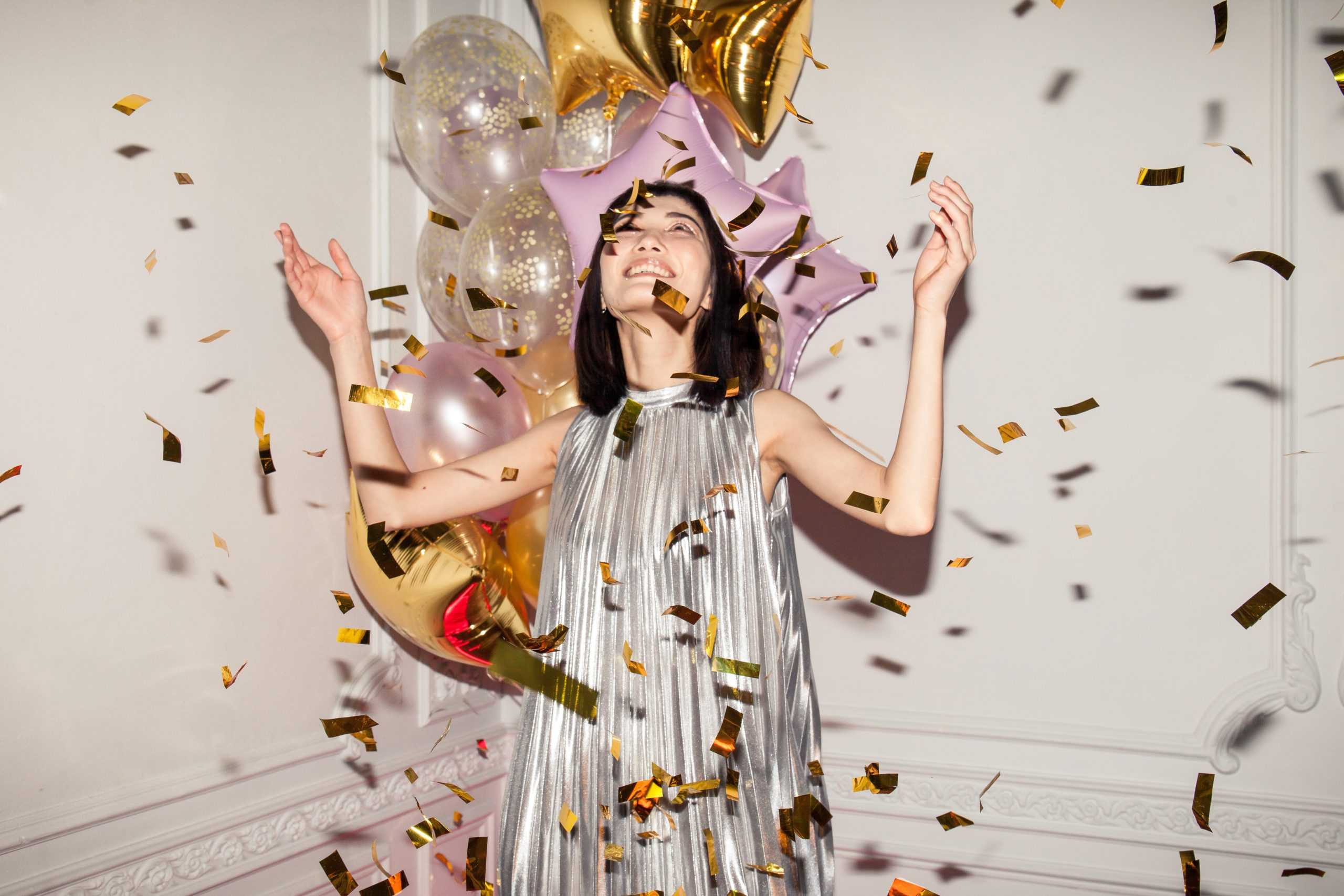 a woman in a silver dress surrounded by confetti and balloons.