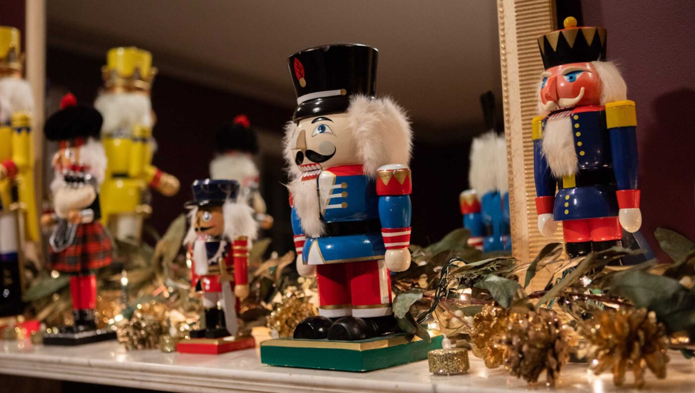 Several painted wooden nutcracker figurines of different sizes and colors are arranged on a decorated mantel with greenery and gold accents, their images reflected in a mirror—capturing the festive spirit of the Christmas in Salem House Tour.