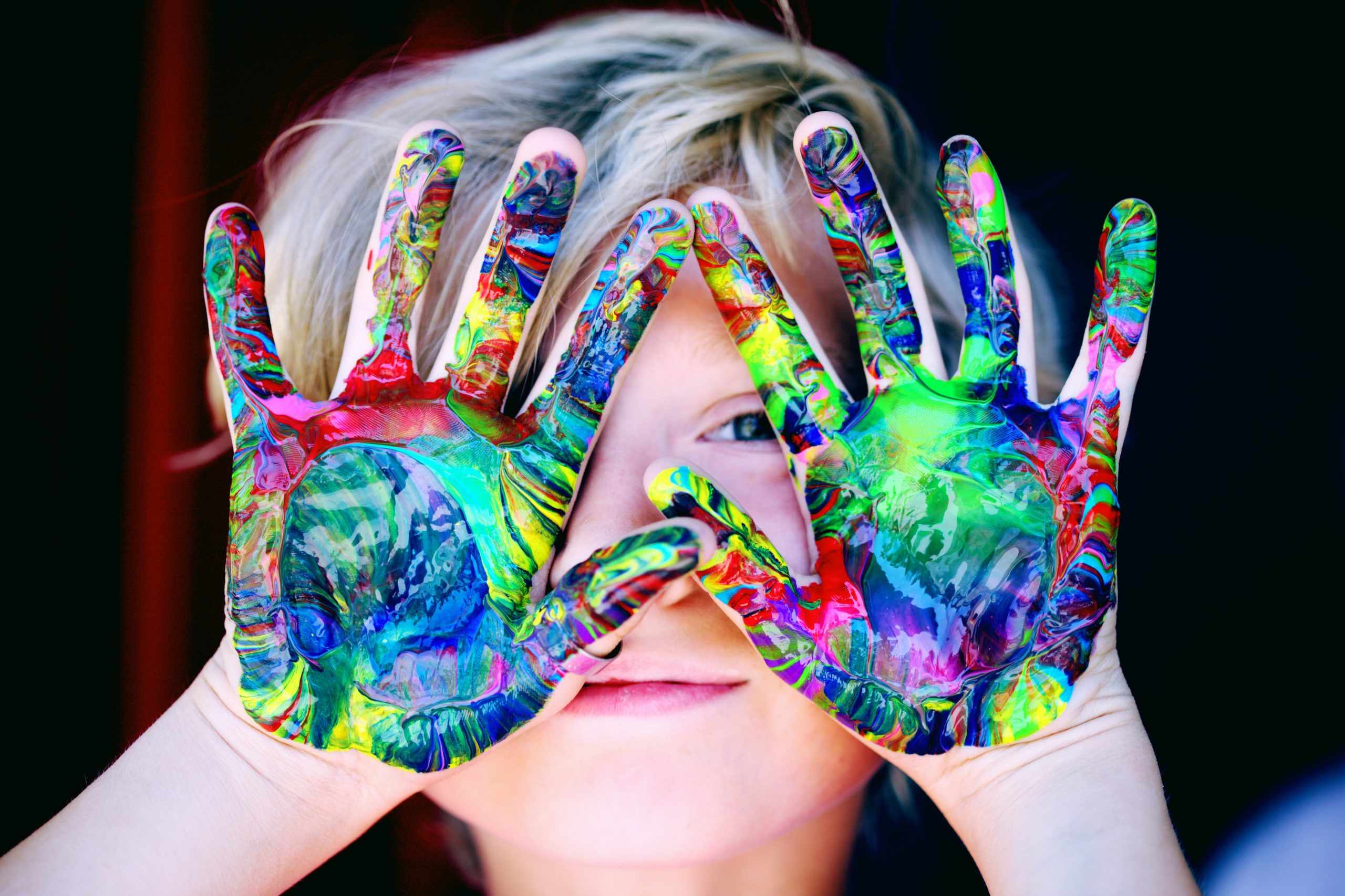 a young girl with painted hands covering her eyes.