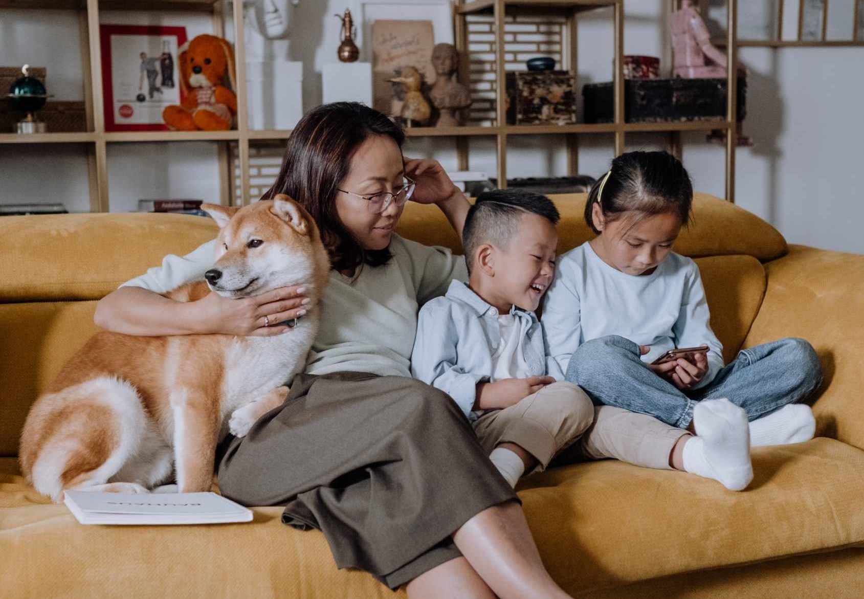 three humans and a dog (left). Mom sits middle, two kids sit to the eight on a yellow couch.