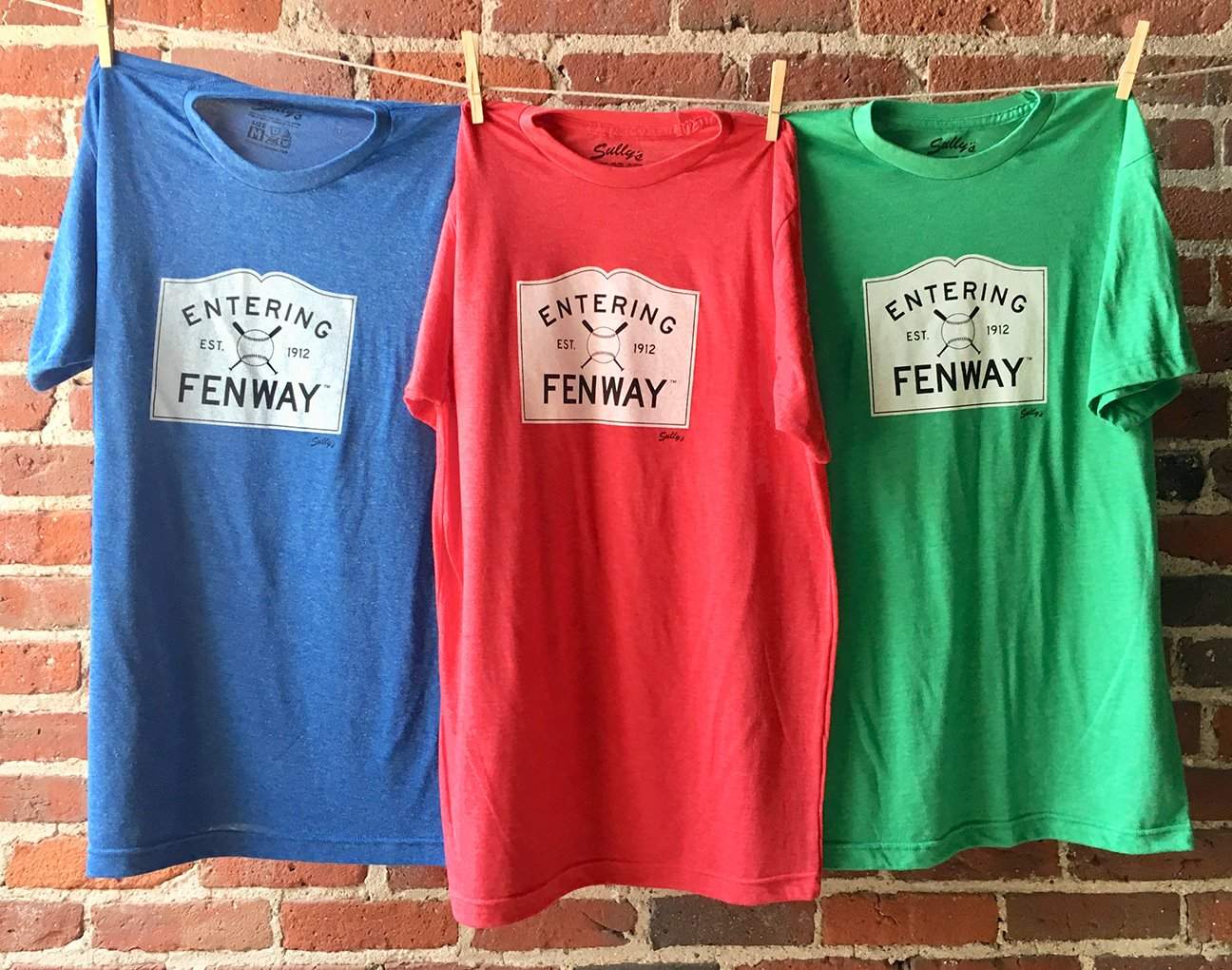 three t - shirts hanging on a brick wall.