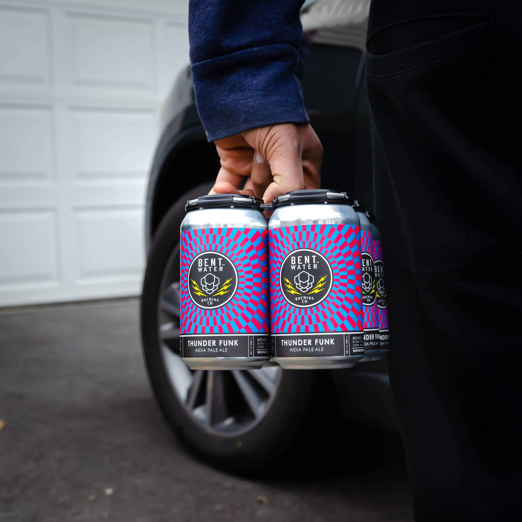 a person holding two cans of beer in front of a car.