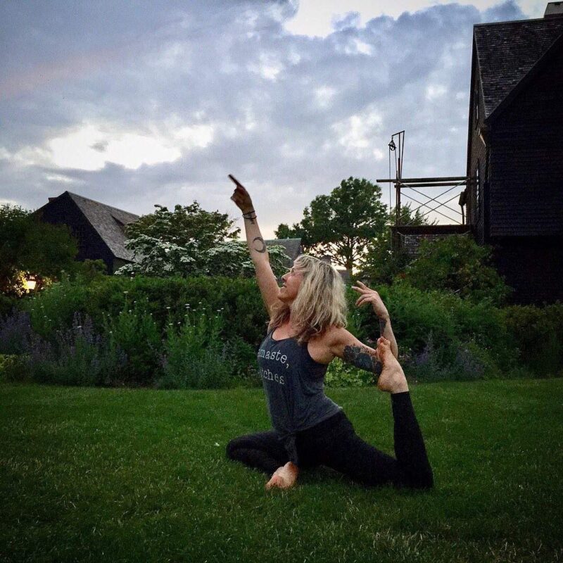 a woman sitting in the grass with her arms in the air.