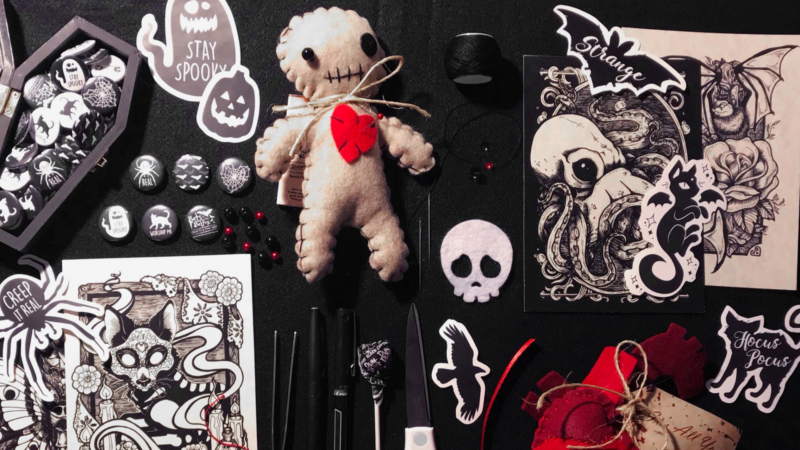 Discover our Halloween collection at Bats in the Belfry Crafts. Unearth a sinister voodoo doll, spooky illustrations, unique buttons, and eerie black ribbons. Plus, explore peculiar scissors and decorative cards—all beautifully arranged on a dark backdrop. Perfect for adding a haunting touch to your seasonal decor!