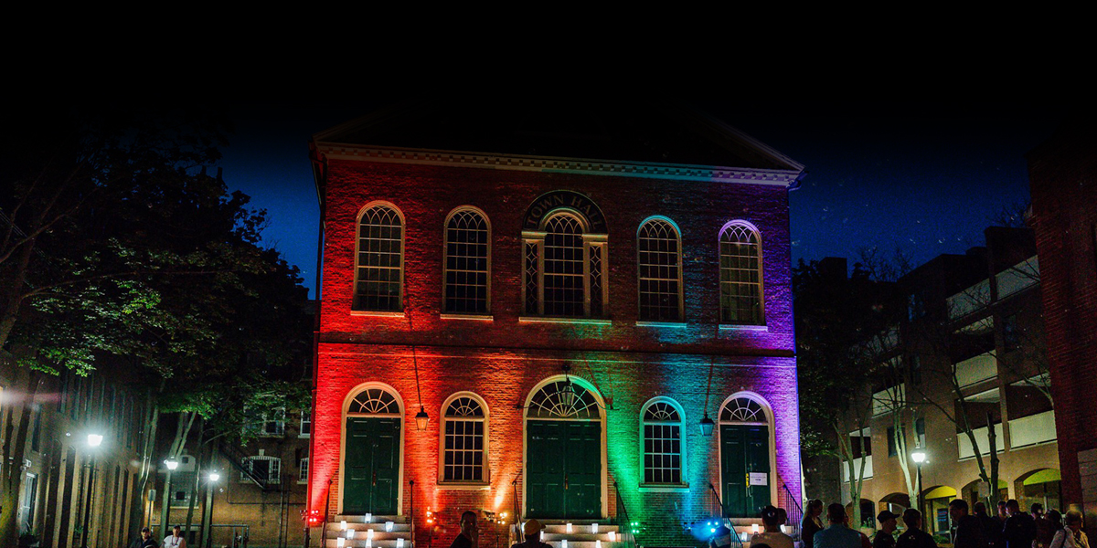the exterior of salem's old town hall is lit with rainbow uplighting at night
