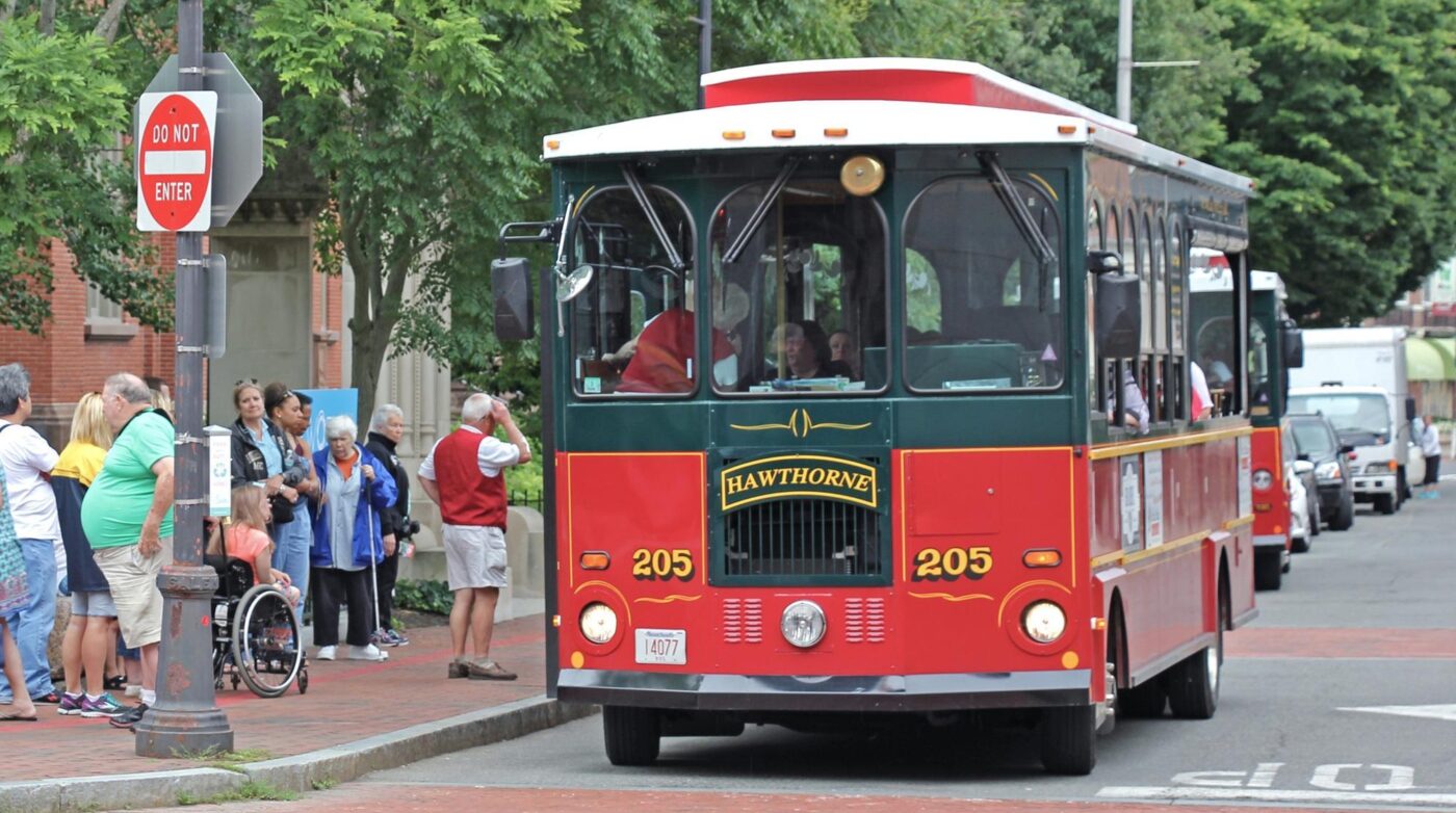 A red and green trolley is driving down the street.