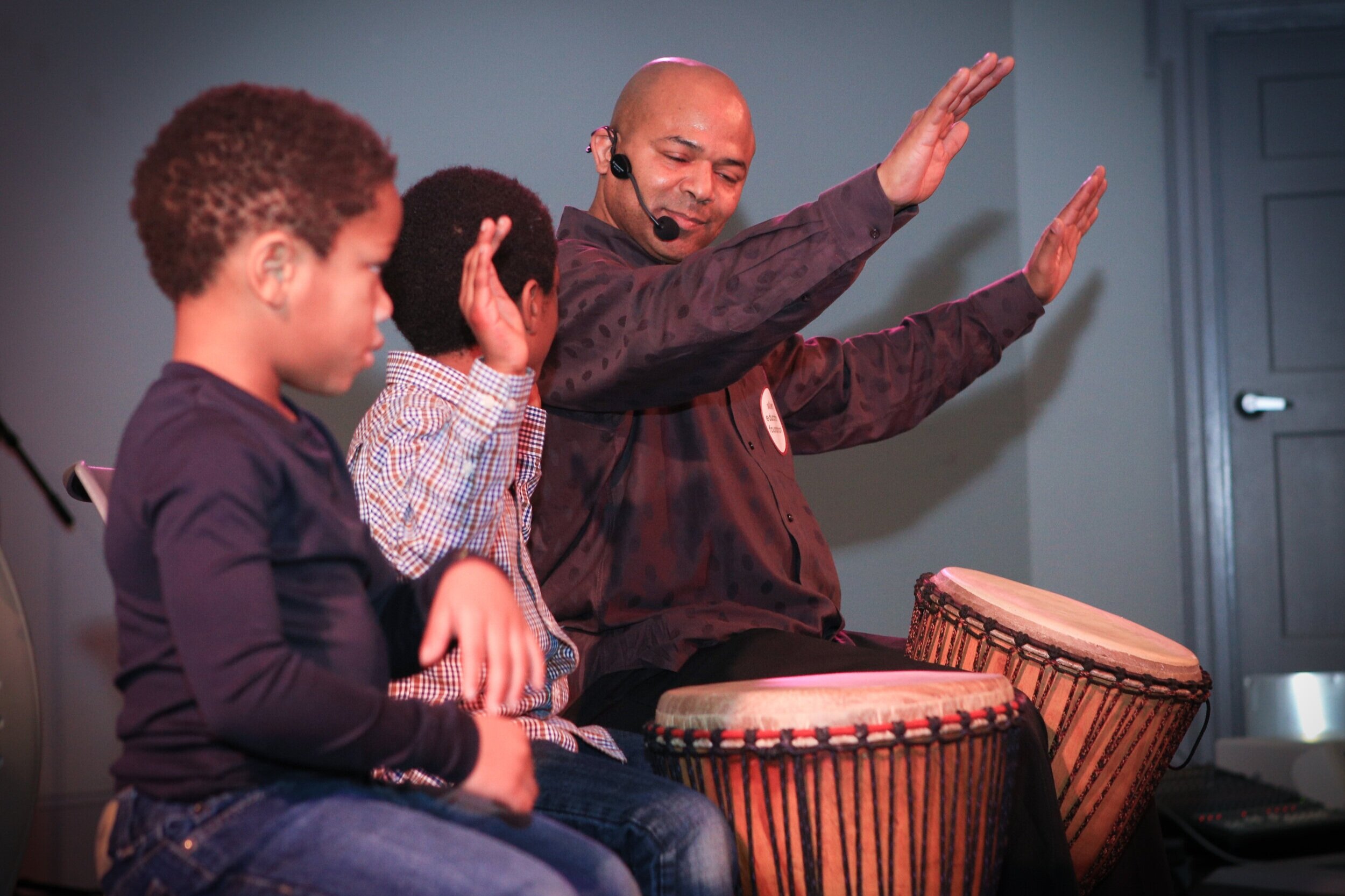 a man and two children are playing with a drum.