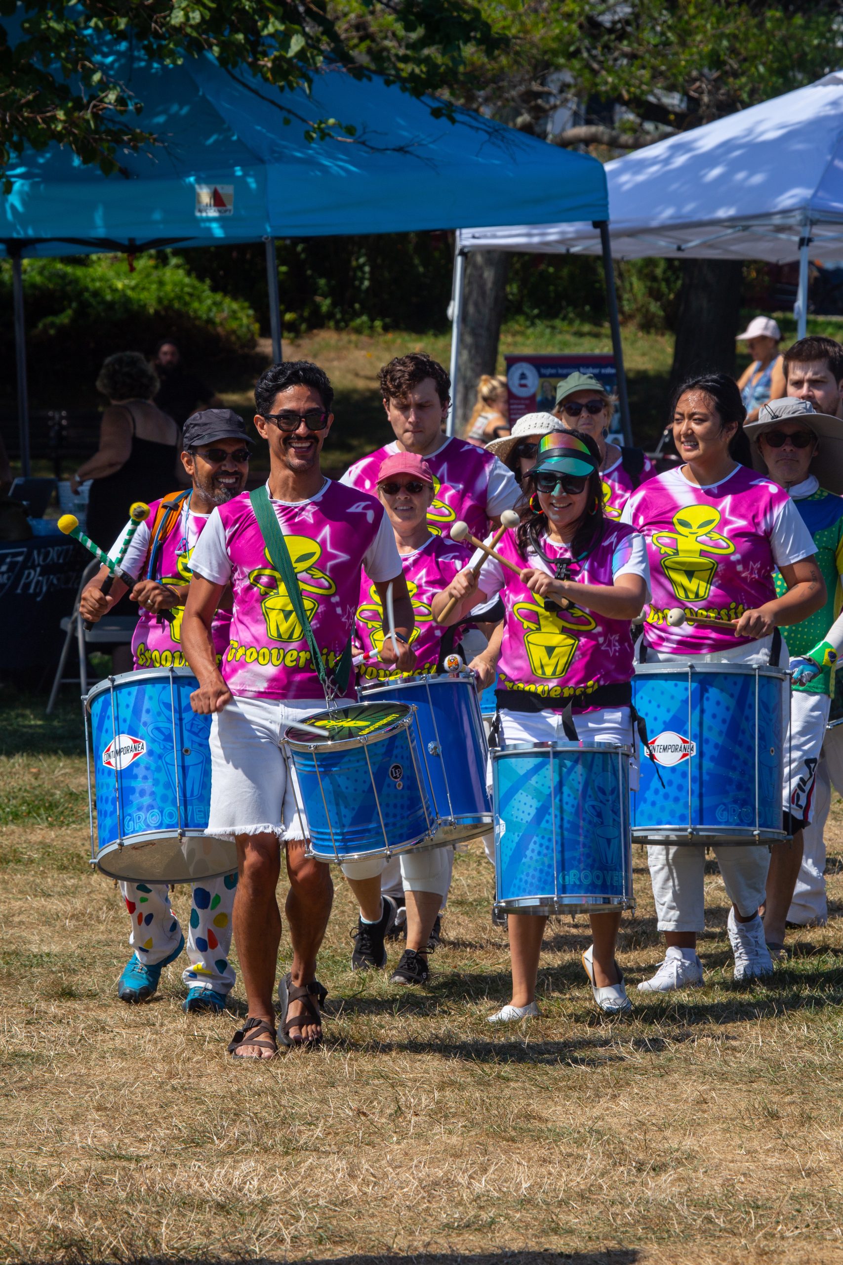 a group of people wearing pink shirts and holding drums performs at the 2022 Diversity Matters Festival