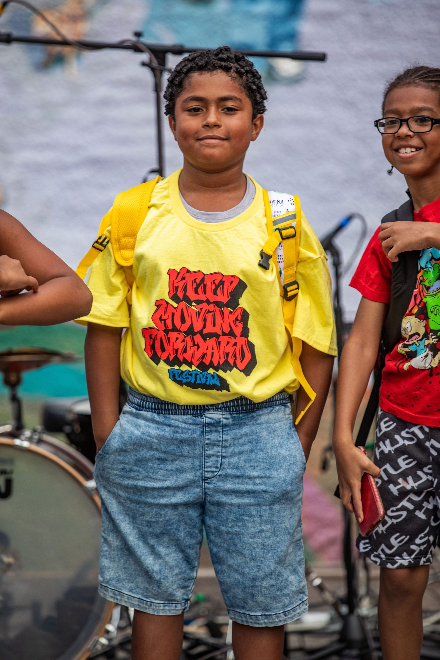 Young performer of color wearing a yellow shirt with red letters that reads "keep moving forward" 