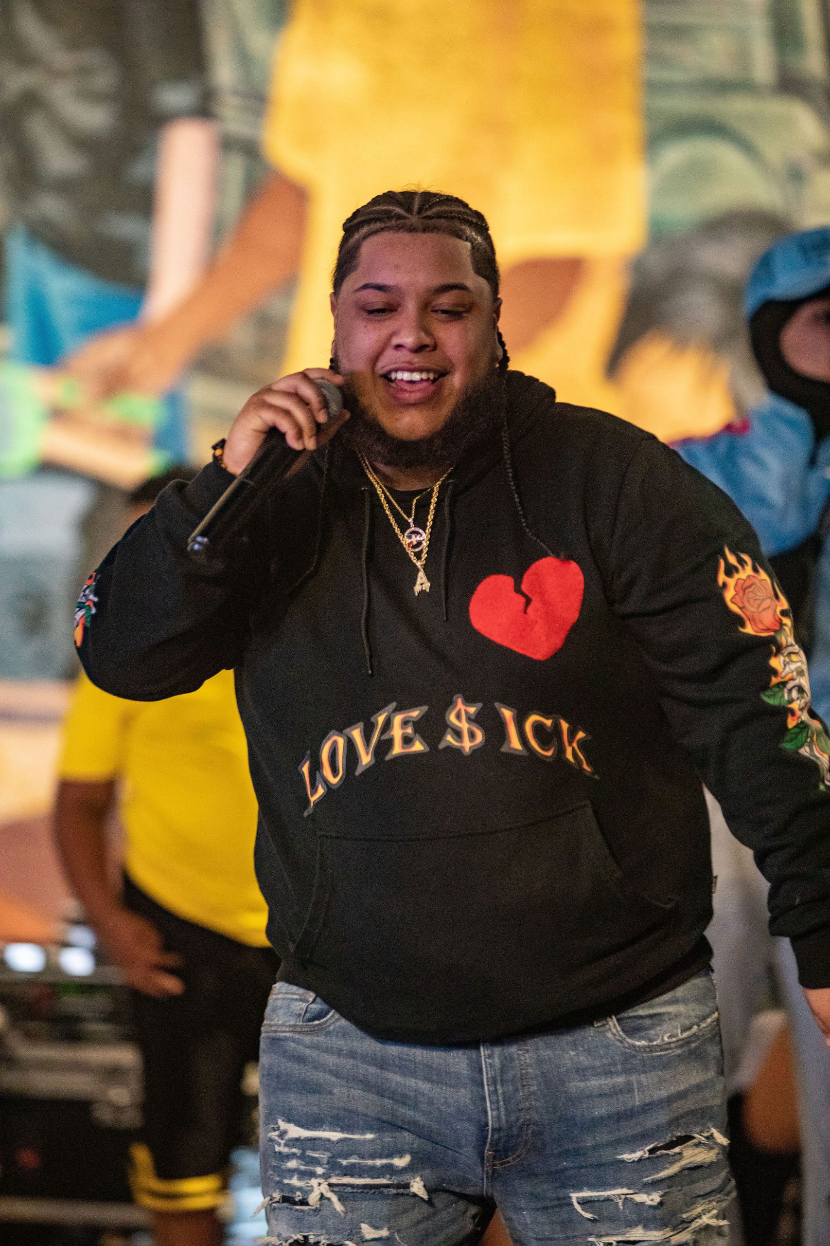 A black performer wears a black sweater that reads Love$ick