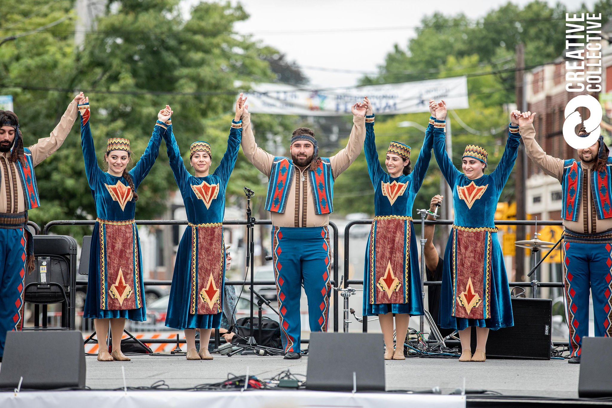 a group of 5 performers in elaborate blue traditional clothing hold hands with arms up at the end of a performance on stage at the peabody international festival 