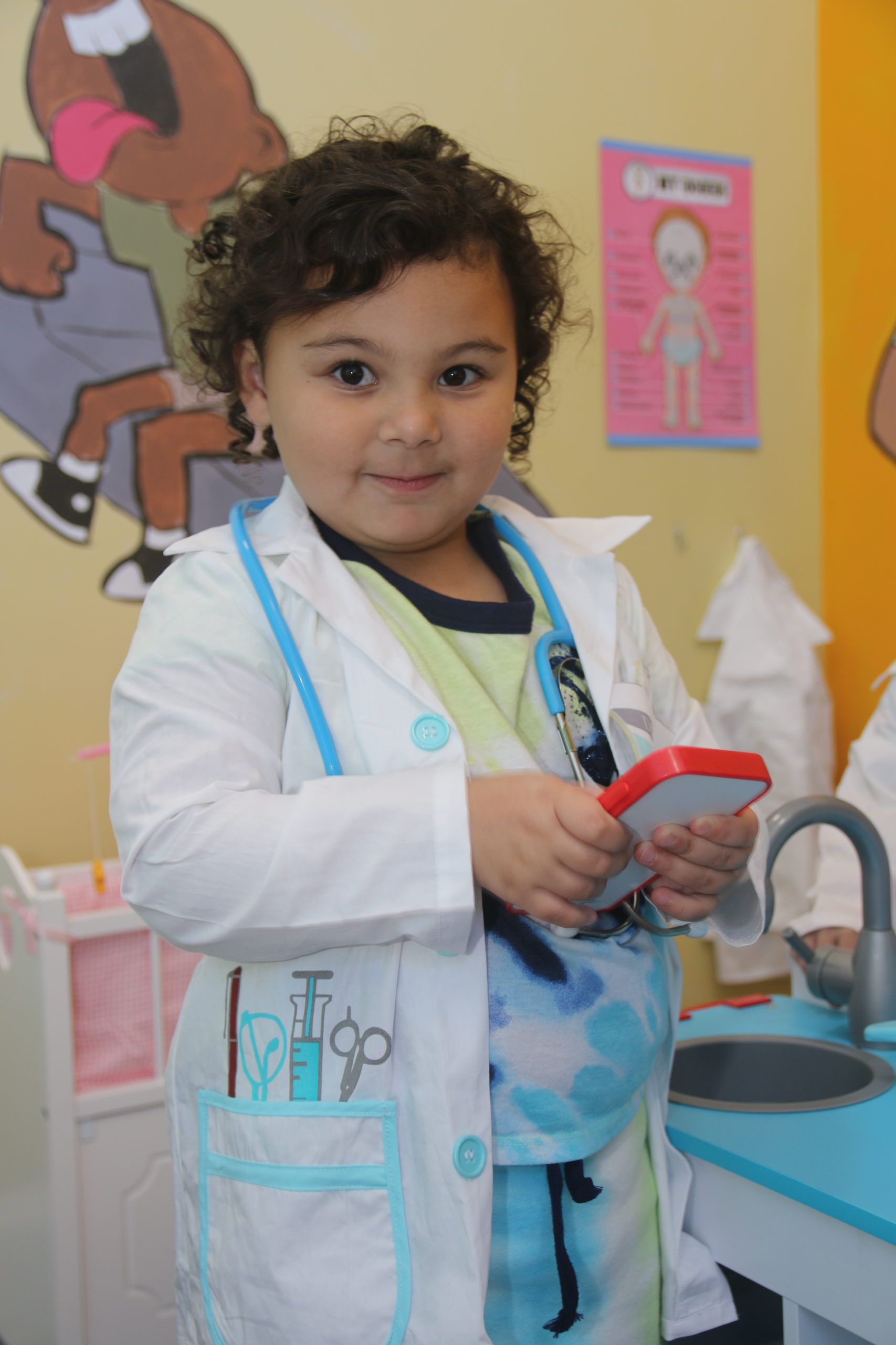 a little girl in a doctor's coat playing with a toy.