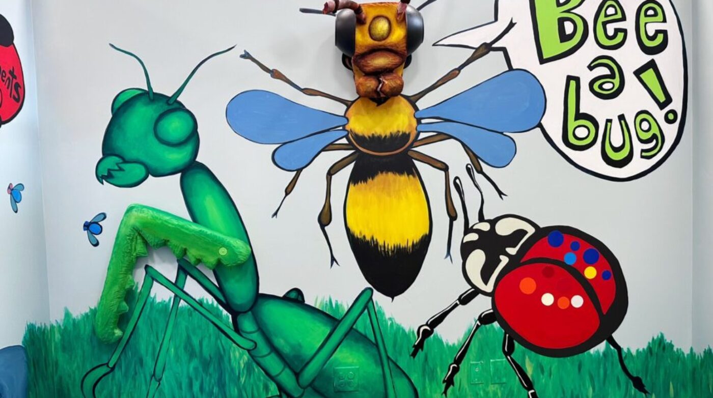 Experience an enchanting wall mural with vibrant colors that showcases a large bee, praying mantis, and ladybug. The playful artwork encourages everyone to "bee a bug!". Perfect for adding a whimsical touch to any space.