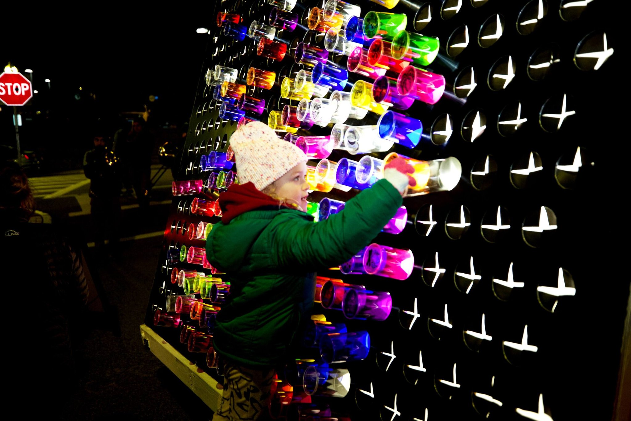 Image of small child wearing a winter coat and hat, reaching for the light peg board which make up the Brighter Ignited art installation.