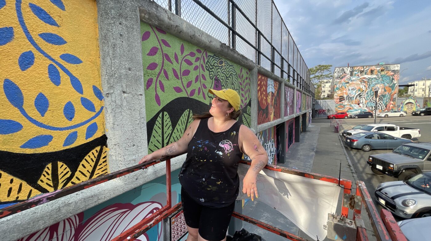 a woman leaning on a fence next to a mural.