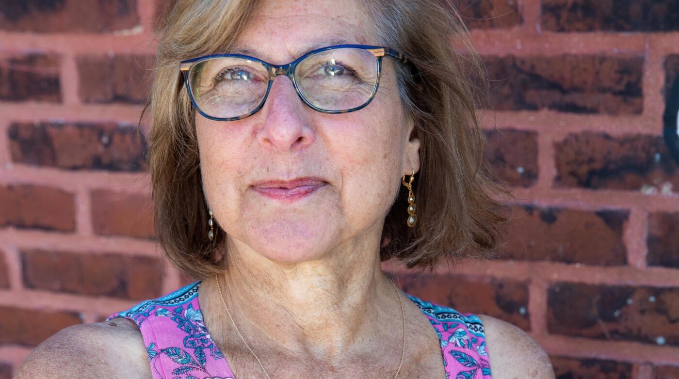 a woman wearing glasses standing in front of a brick wall.