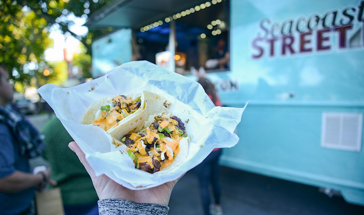 a person holding up a taco in front of a food truck.