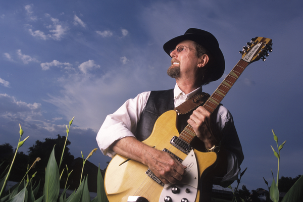 a man in a hat and vest playing a guitar.