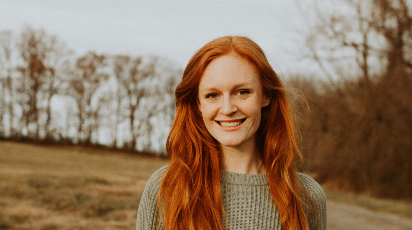 a woman with red hair standing in a field.
