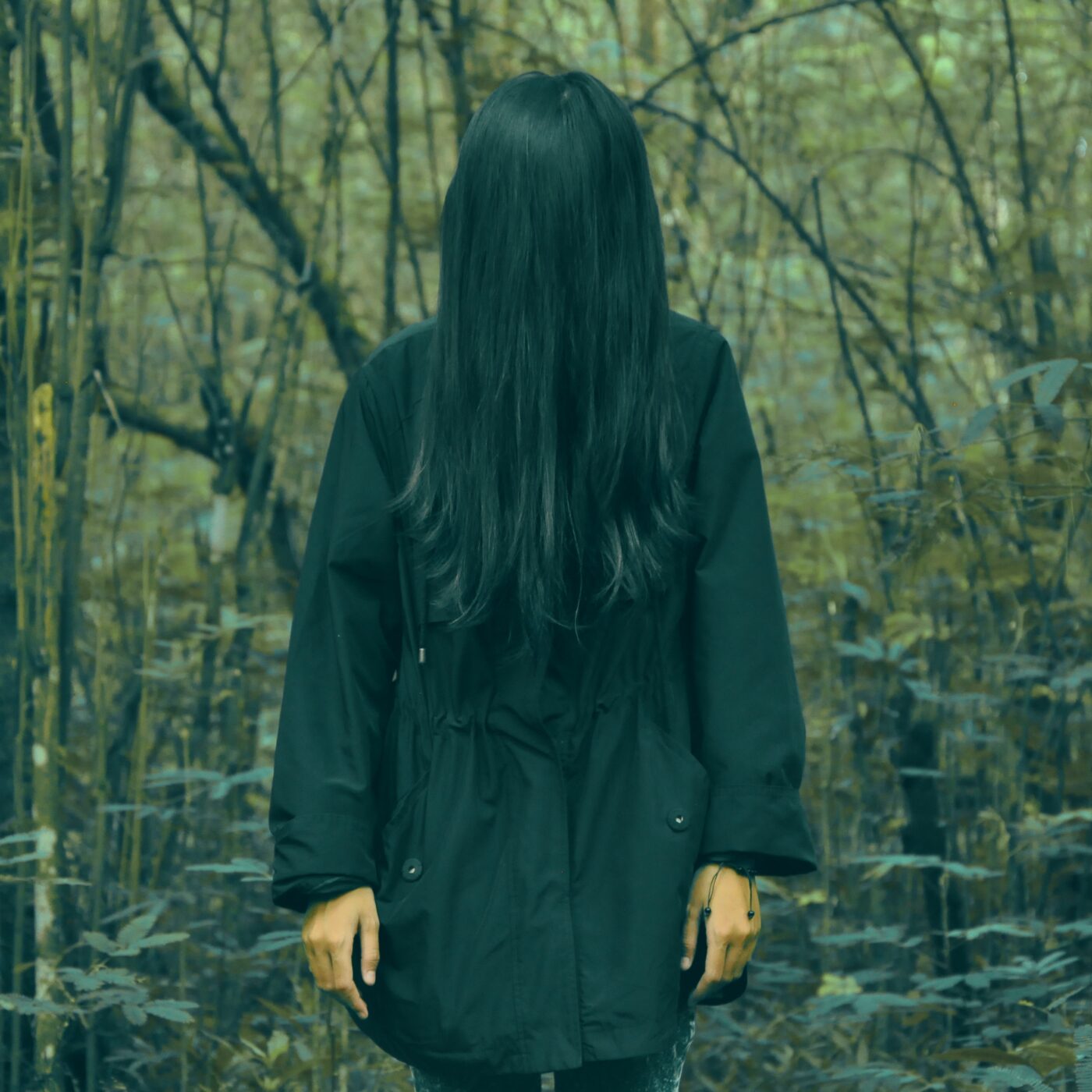 a woman with long black hair standing in a forest.