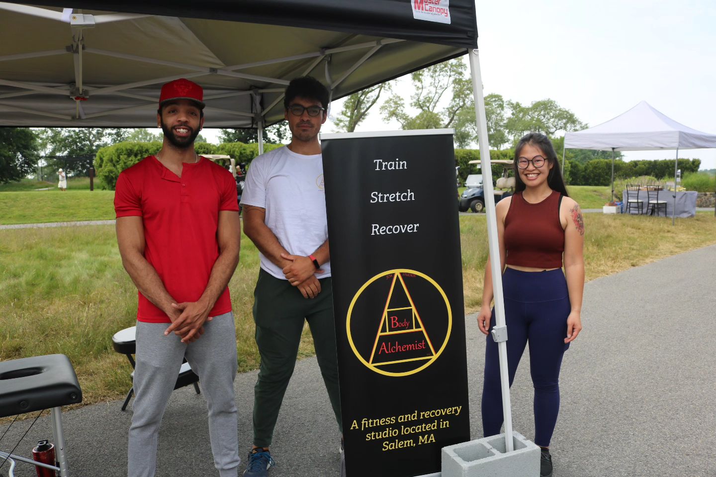 Three Body Alchemist employees pose under a tent with a sign.