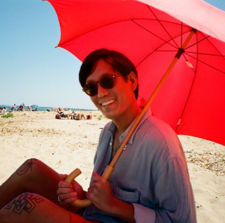 a man sitting on the beach holding a red umbrella.