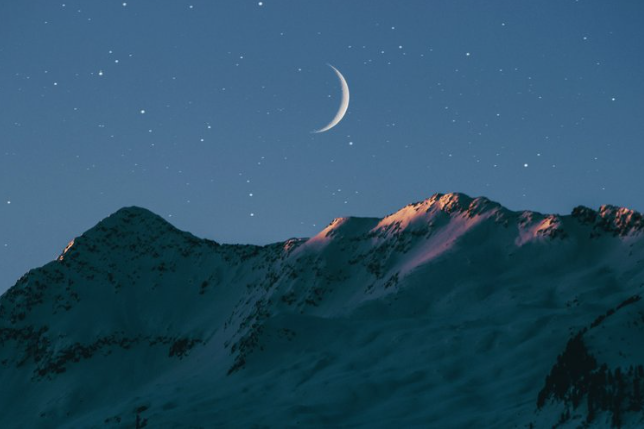 the moon is shining over a snowy mountain.