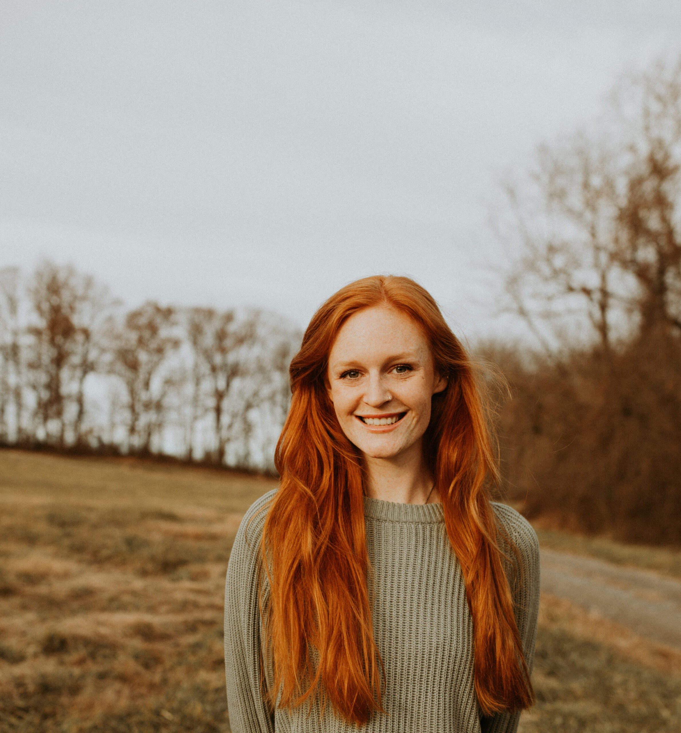 a woman with red hair standing in a field.