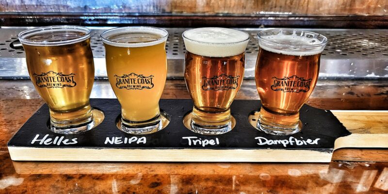 four beers are lined up on a wooden board.