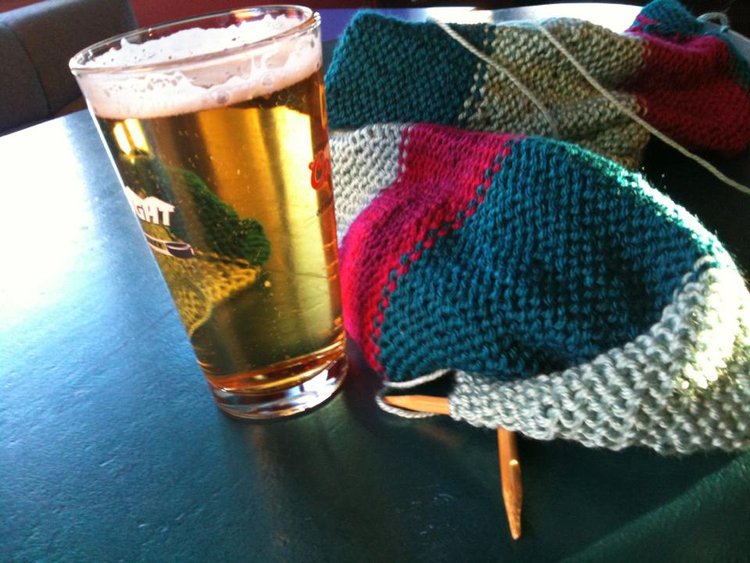 a glass of beer on a table next to a knitted hat.