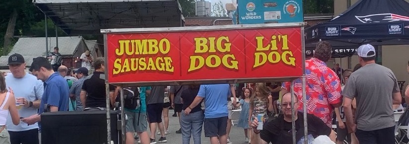 A group of people standing near a sign that says jumbo big big sausage dog.