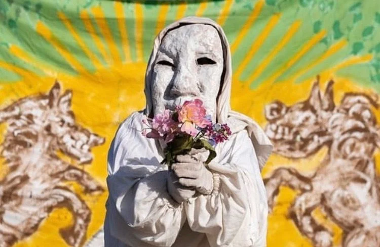 A person dressed in white holding flowers in front of a mural.