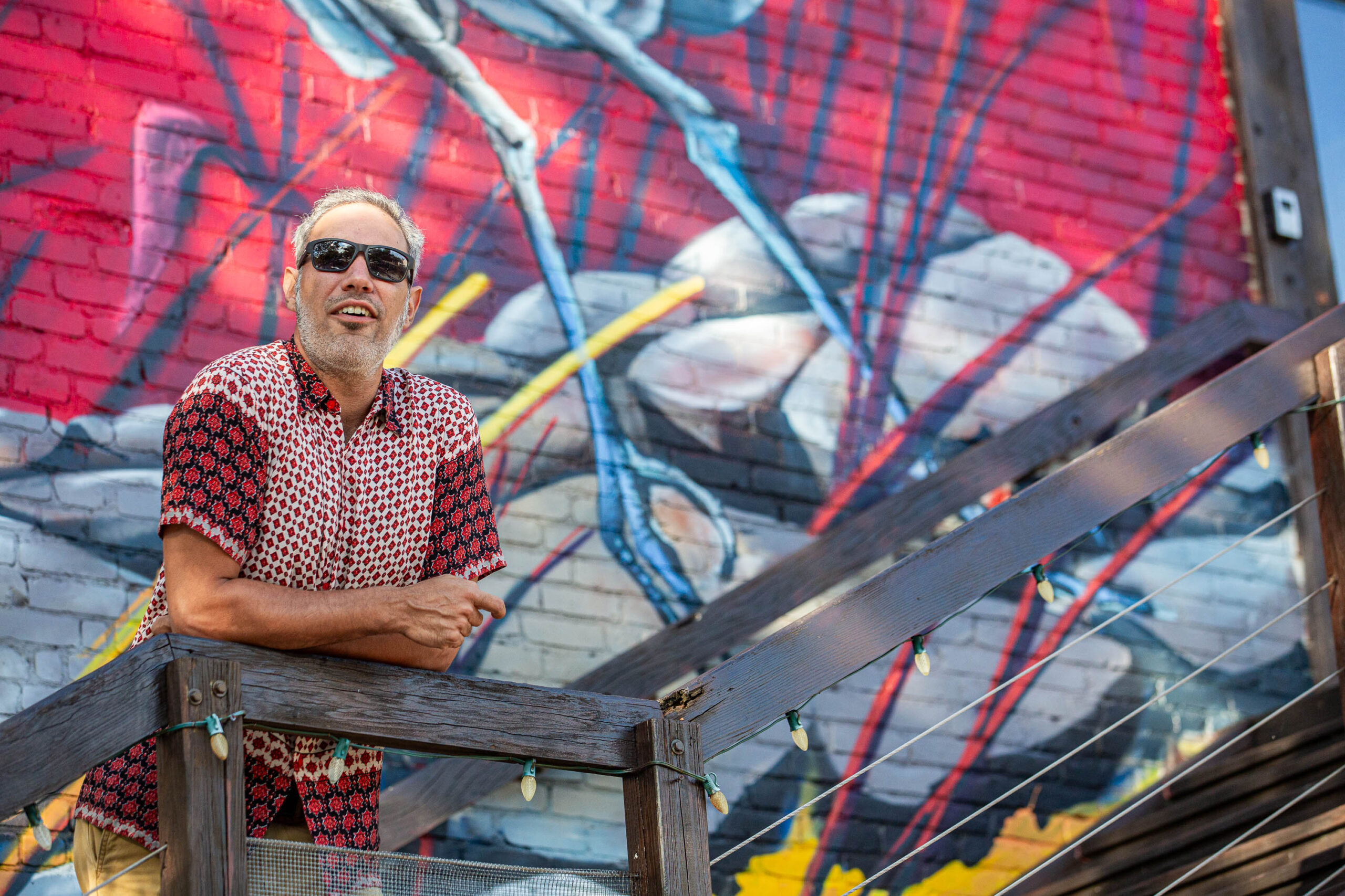 A man in sunglasses standing next to a mural.