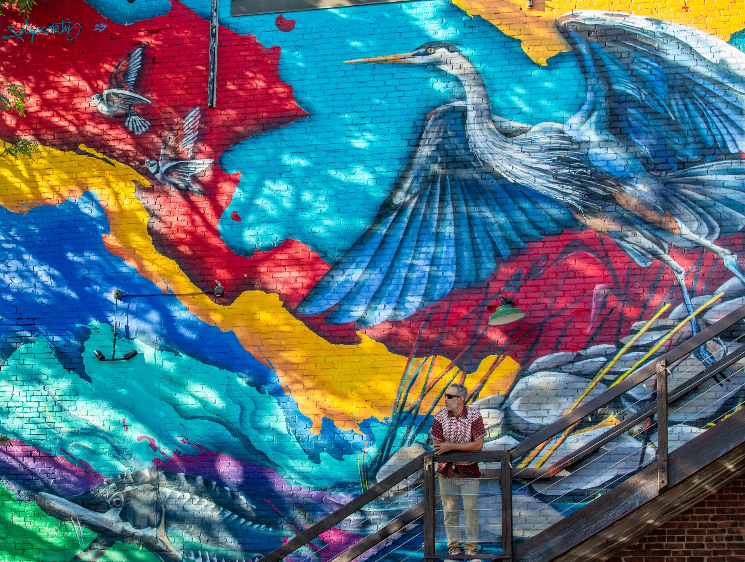 A woman standing in front of a colorful mural.