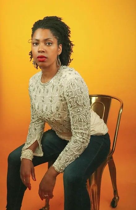A woman in jeans and a white top sitting on a chair.
