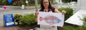 A woman holding up a painting of a fish.