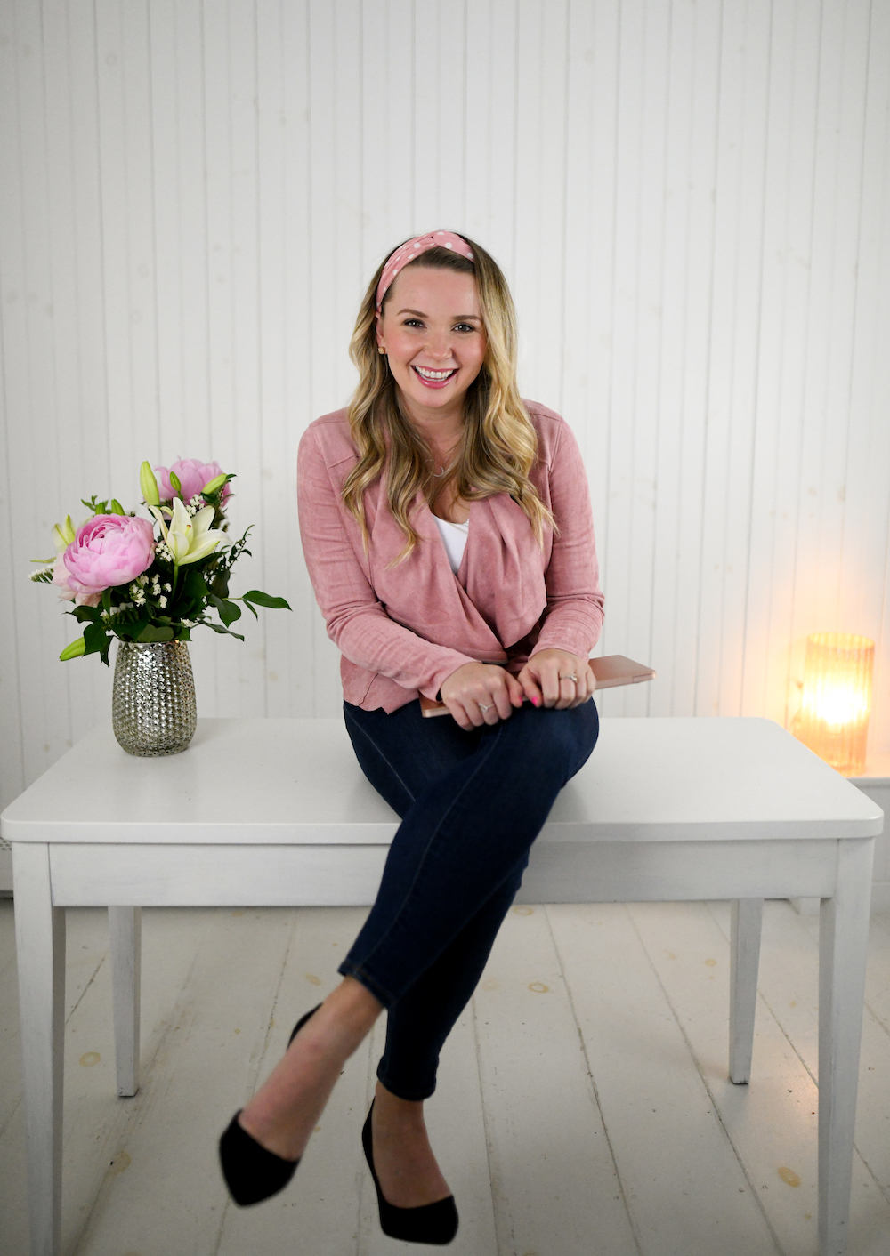 A blonde woman sitting on a white table with flowers.