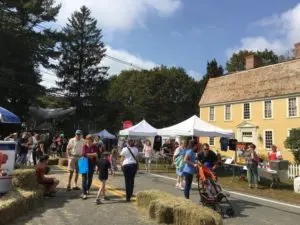 A crowd of people at a farmers' market in front of a house.