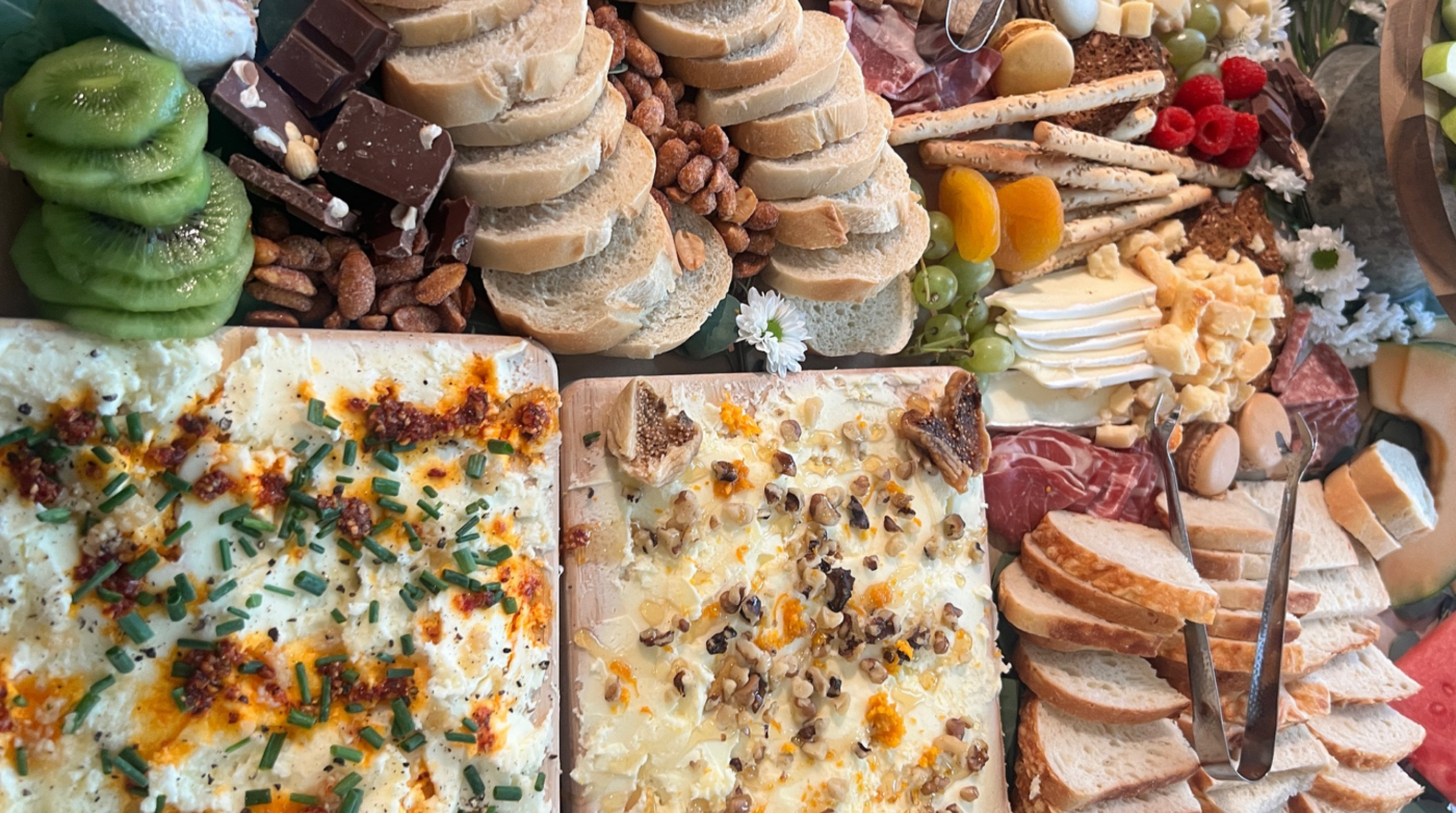 Indulge in a charcuterie board packed with handpicked delights: a tasty mix of cheeses, meats, fresh bread, juicy kiwi and grapes, crunchy nuts, rich chocolate, and crispy crackers. Each bite is an invitation to savor new flavors.