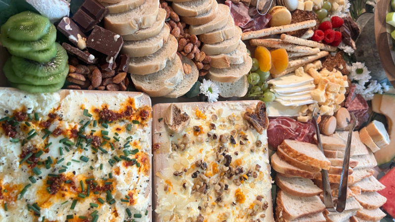 Indulge in a charcuterie board packed with handpicked delights: a tasty mix of cheeses, meats, fresh bread, juicy kiwi and grapes, crunchy nuts, rich chocolate, and crispy crackers. Each bite is an invitation to savor new flavors.